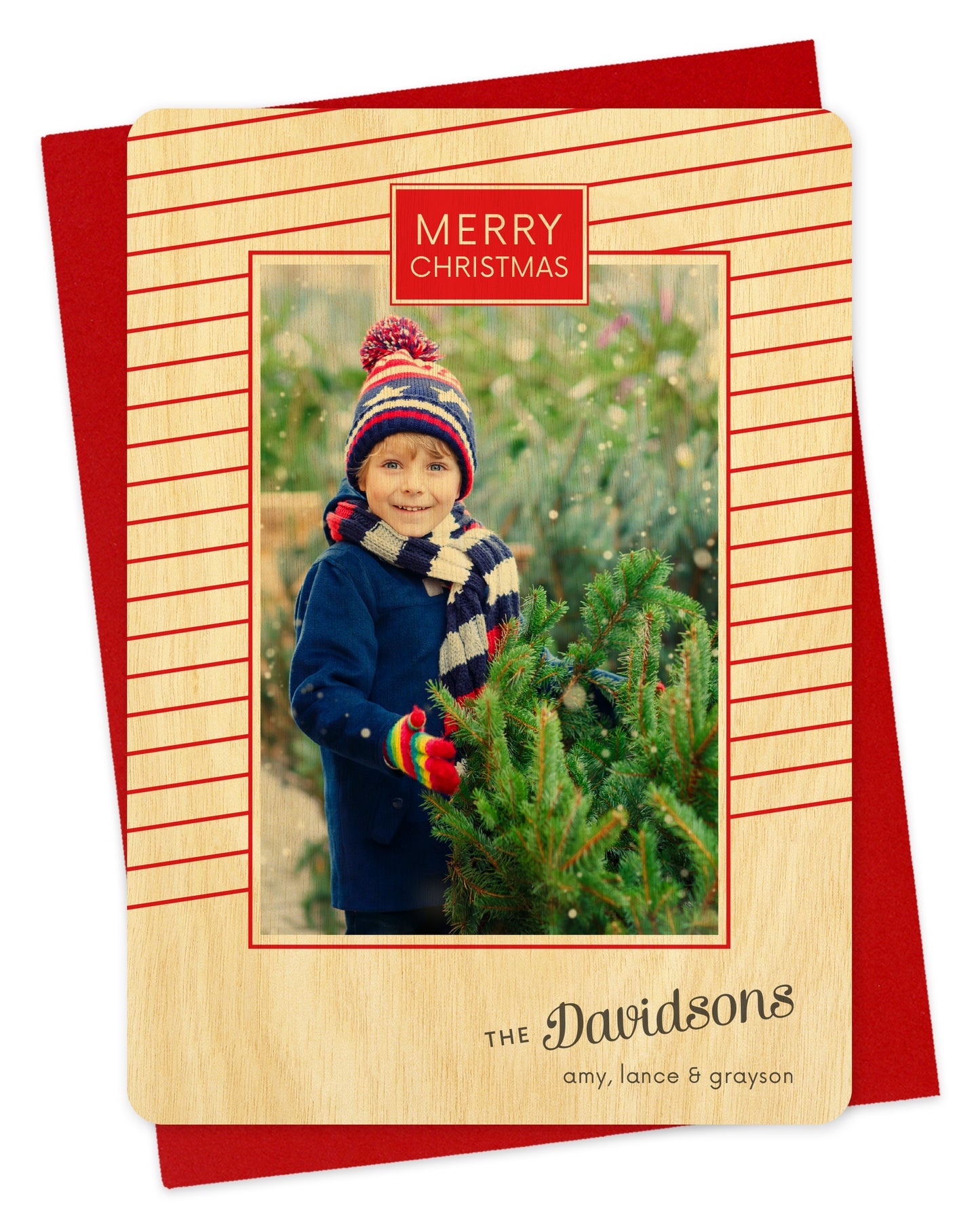 Customizable wood holiday card featuring a photo bordered by thin, diagonal red stripes, “MERRY CHRISTMAS” text near the top and a personal greeting near the bottom. Shown with a red envelope.