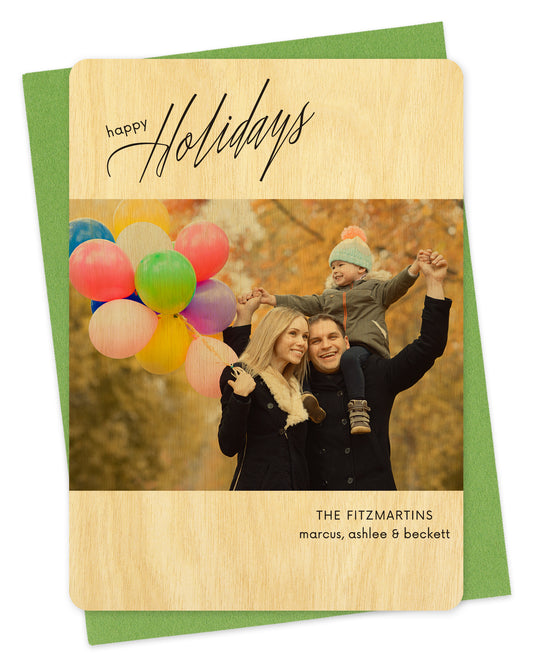 Customizable wood holiday card featuring your photo bordered by birch wood with black "Happy Holidays" text near the top and your personal greeting at the bottom. Shown with a green envelope.