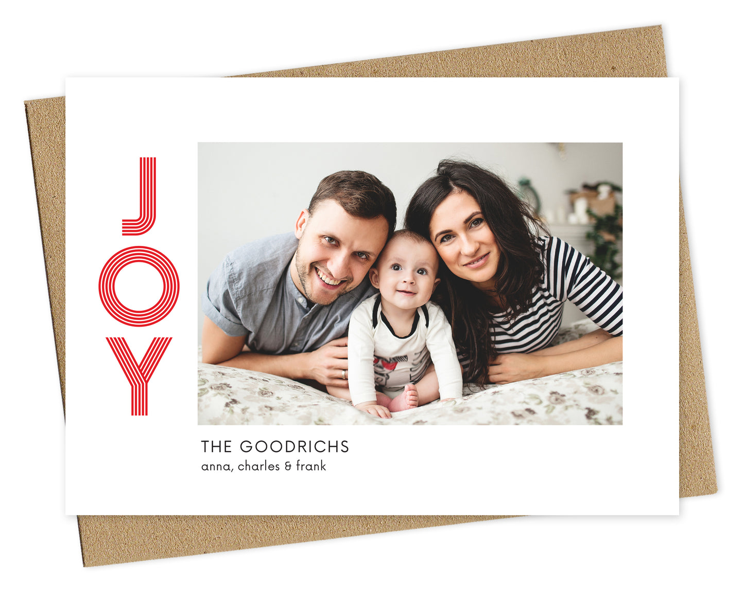 Customizable paper holiday card featuring your photo bordered by white with the word "JOY" in red on the left and a personal greeting in black on the bottom. Pictured with a kraft envelope.