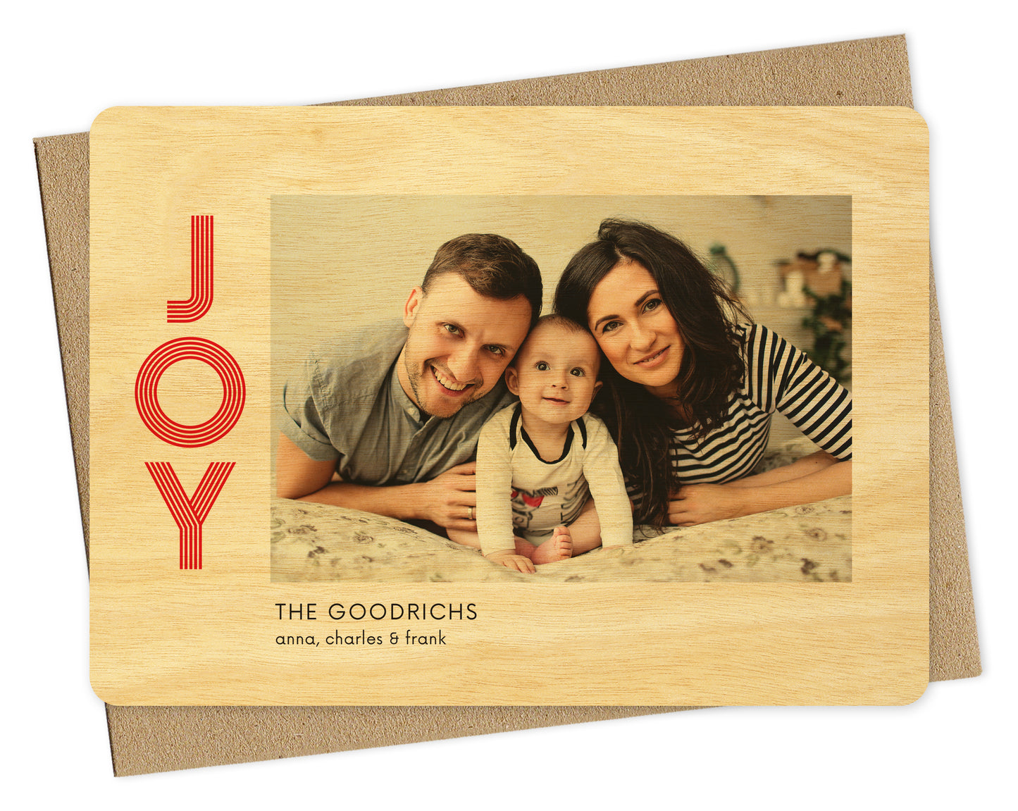 Customizable wood holiday card featuring your photo bordered by birch wood grain with the word "JOY" in red on the left and a personal greeting in black on the bottom. Pictured with a kraft envelope.
