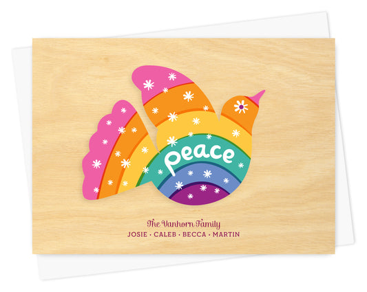 Customizable paper holiday card with a colorful rainbow dove, “Peace” sentiment and personal message on a printed birch wood grain background. Shown with a white envelope.