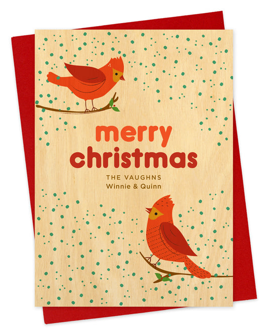 Customizable paper Christmas card featuring two red cardinals perched against a snowy background with “Merry Christmas” text and a personal greeting. Shown with a red envelope.