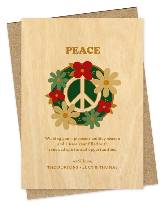 Customizable paper holiday card with a printed birch wood grain background. Card design features a peace sign surrounded by colorful flowers with “Peace” text at the top and a personal greeting at the bottom. Shown with a kraft envelope.