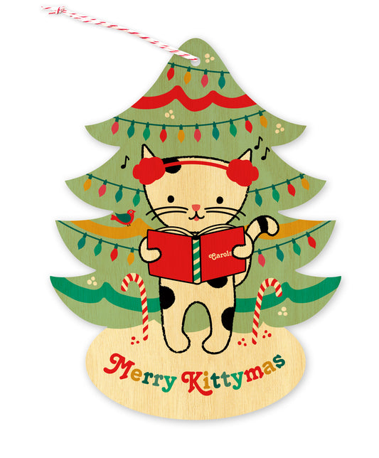 Front of a tree-shaped wood holiday ornament card featuring a cat in earmuffs singing carols in front of a decorated Christmas tree on a natural birch wood background. 