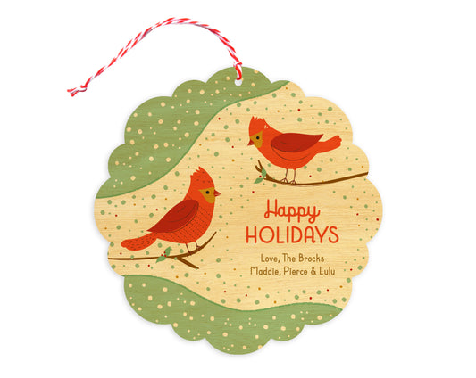 Front of customizable birch wood holiday ornament card featuring a pair of red birds perched on branches, "Happy Holidays" text, a personal message and a snowy backdrop. Round ornament with scalloped edges.