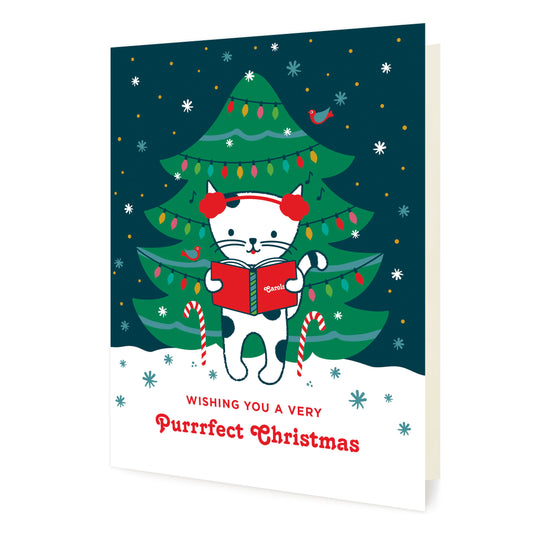Front of folded Christmas card featuring a cat in earmuffs singing carols in front of a decorated Christmas tree and snowy skies outside with the pun “Wishing You a Treemendous Holiday.”