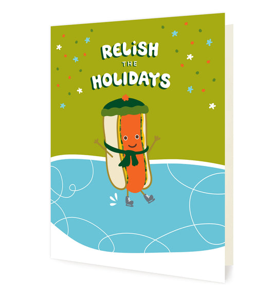 Front of folded card with a cute illustrated hot dog wearing a stocking hat and scarf and ice skating. Card reads “Relish the Holidays” against a snowy green and blue background.