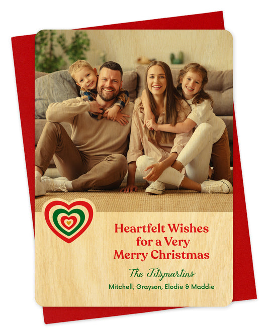 Customizable wood holiday card featuring a family photo, a red and green heart, 'Heartfelt Wishes for a Very Merry Christmas' text and a personal greeting. Shown on a red envelope.