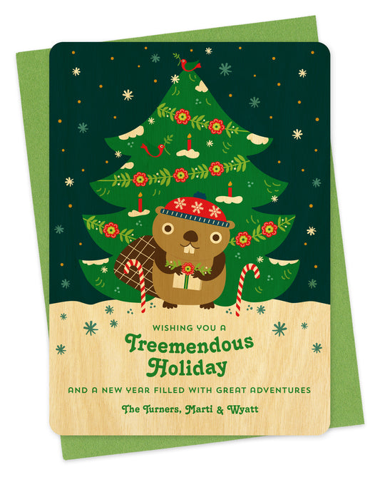 Customizable birch wood holiday card featuring a cute beaver holding a gift in front of a decorated outdoor Christmas tree, "Wishing you a Treemendous Holiday" text and a personal greeting at the bottom. Shown with a green envelope.