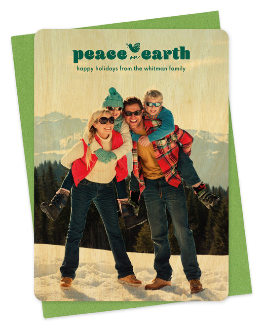 Customizable wood holiday card featuring a full portrait photo with the words “Peace on Earth” and a dove carrying an olive branch near the top, shown with a green envelope.