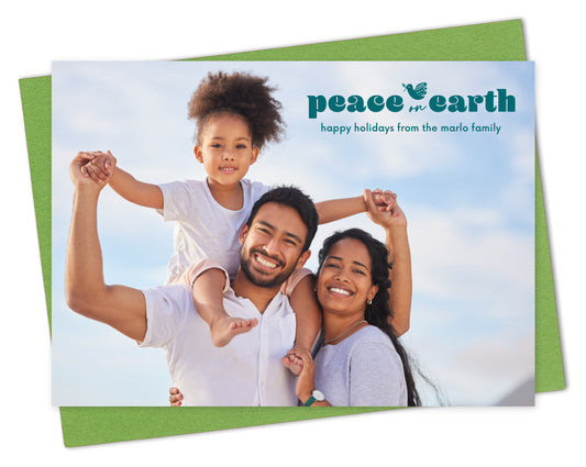 Customizable wood holiday card featuring a full landscape photo with the words “Peace on Earth” and a dove carrying an olive branch near the top, shown with a green envelope.
