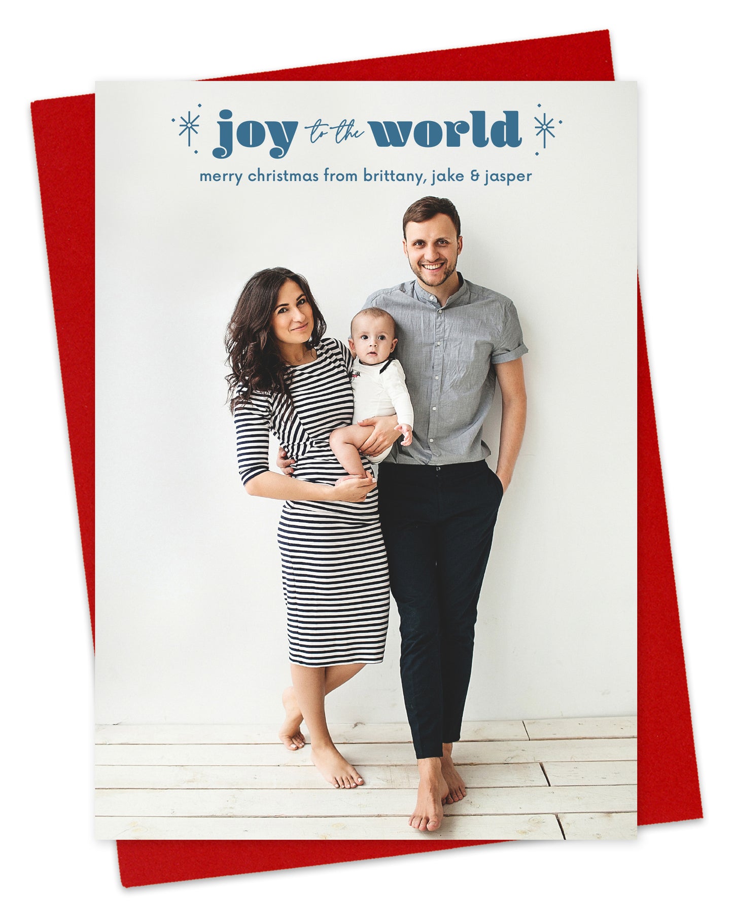 Customizable paper holiday card featuring a full portrait photo with "joy to the world” text and sparkle illustrations near the top, shown with a red envelope.