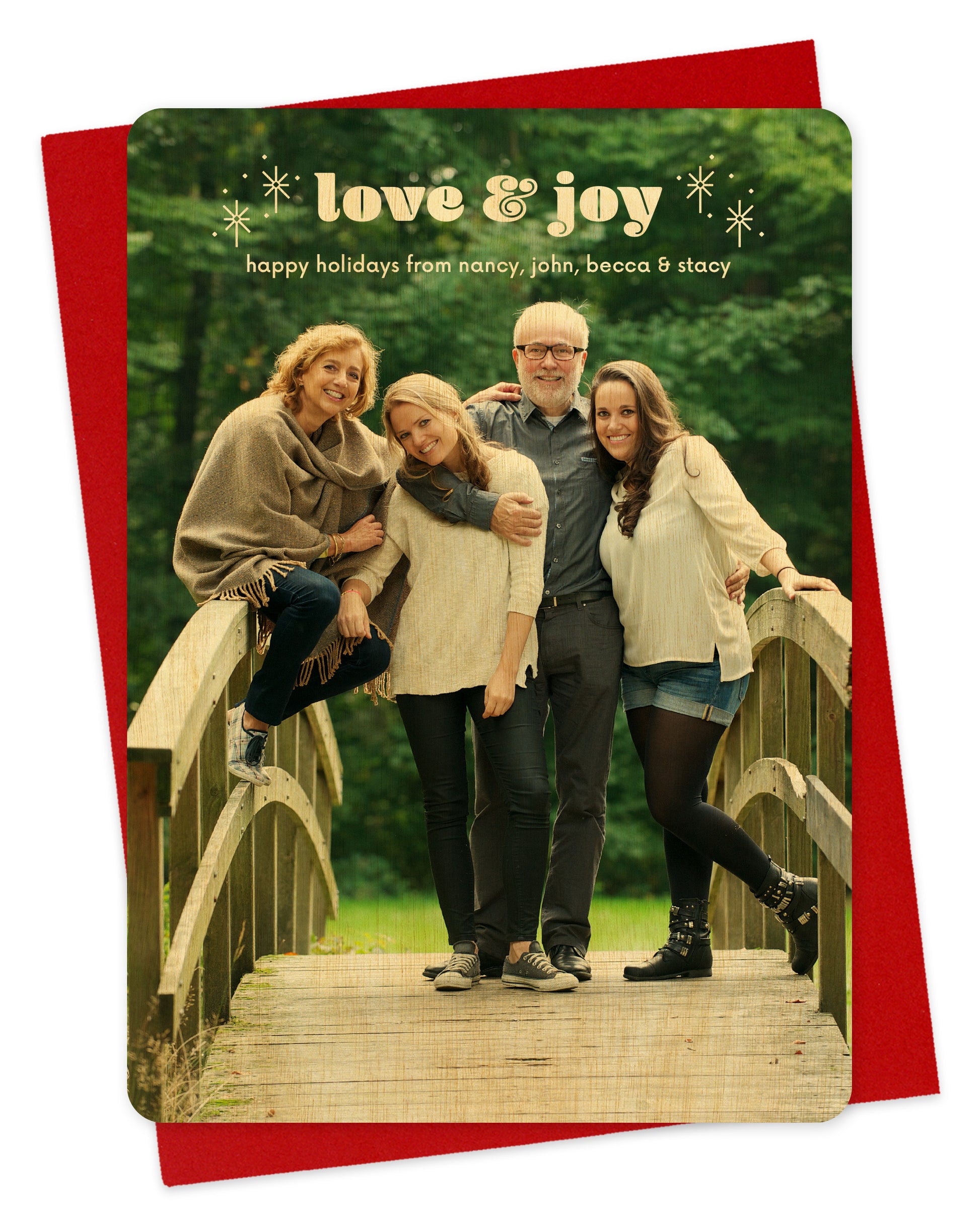 Customizable wood holiday card featuring a full photo with "love & joy” text and sparkle illustrations near the top, shown with a red envelope.
