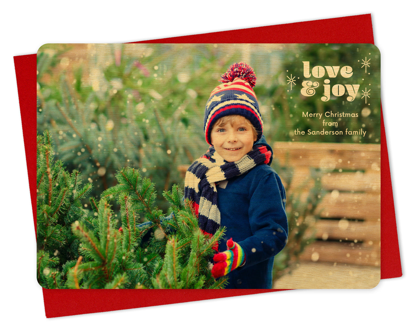 Customizable wood holiday card featuring a full landscape photo with "love & joy” text and sparkle illustrations near the top, shown with a red envelope.
