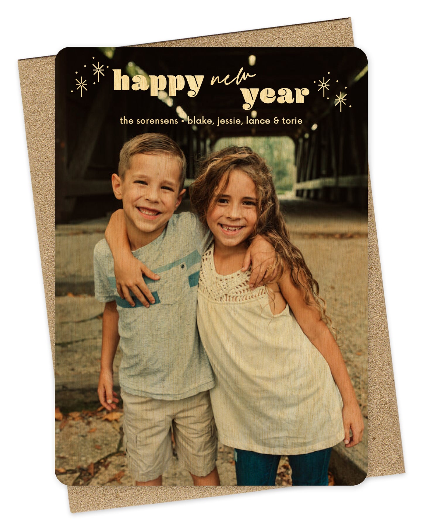 Customizable wood holiday card featuring a full photo with "happy new year” text, sparkle illustration and personal greeting near the top. Shown with a kraft envelope.