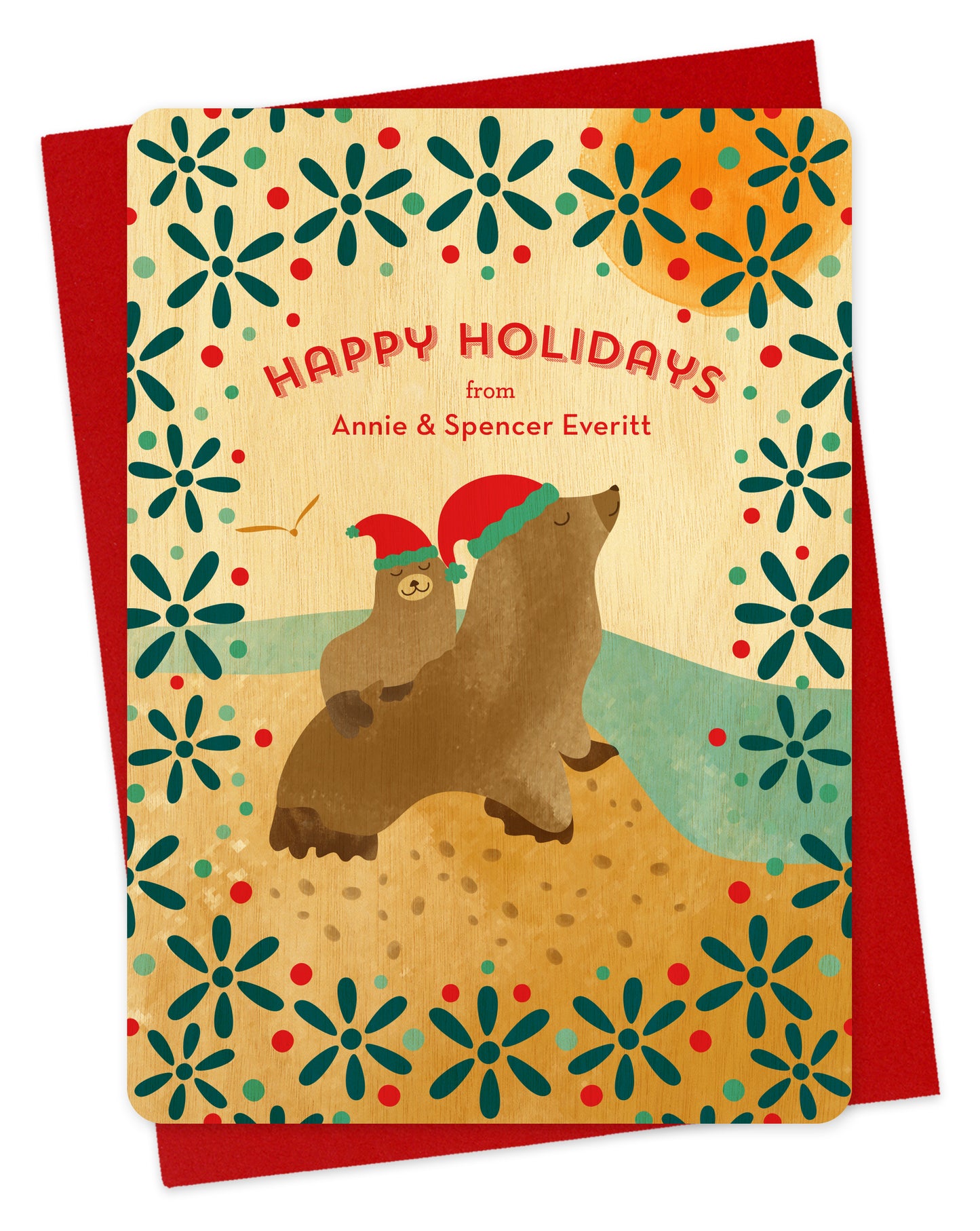Customizable birch wood holiday card featuring two illustrated sea lions in Santa hats, near the water with a festive patterned background. “Happy Holidays” sentiment along with a personal greeting. Shown with a red envelope.