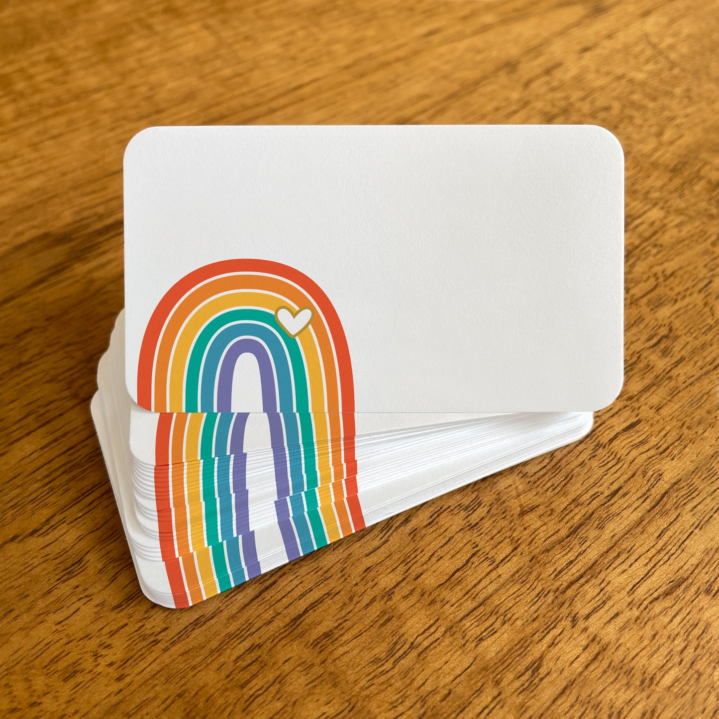 A stack of small white rainbow note cards with rounded corners, featuring a colorful rainbow with an overlapping white heart.