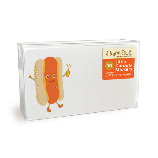 A clear plastic box displaying a small white note card with rounded corners featuring a cute hot dog with a smiling face, arms and legs, wearing sneakers and holding a yellow mustard bottle. The box label reads “Night Owl Paper Goods - 30 - Little Cards & Stickers - Use for Gifts, Lists, Notes.”