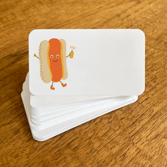 A stack of small white Hot Dog note cards with rounded corners, featuring a cheerful hot dog character with a smiling face, arms and legs, wearing sneakers and holding a yellow mustard bottle.