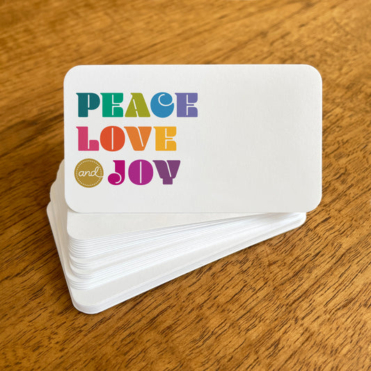 A stack of small white Peace Love Joy note cards with rounded corners, featuring colorful “PEACE LOVE and JOY” lettering in various shades of teal, green, blue, pink, orange, yellow and purple.