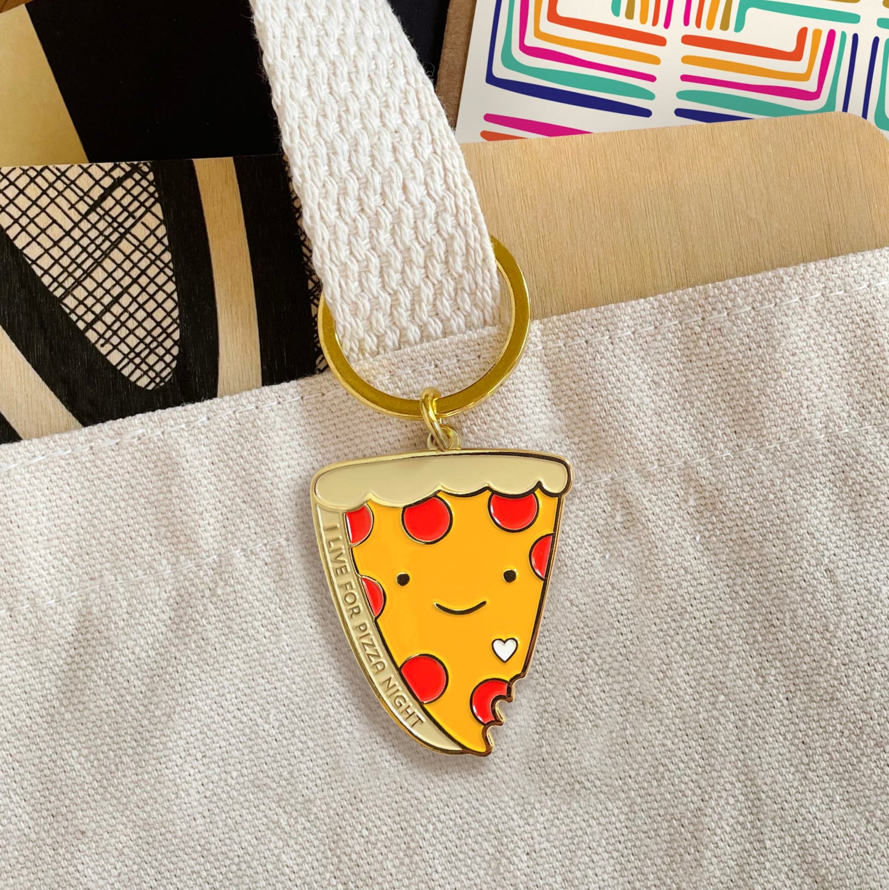 Pizza Night enamel keychain hanging from the handle of a canvas tote bag