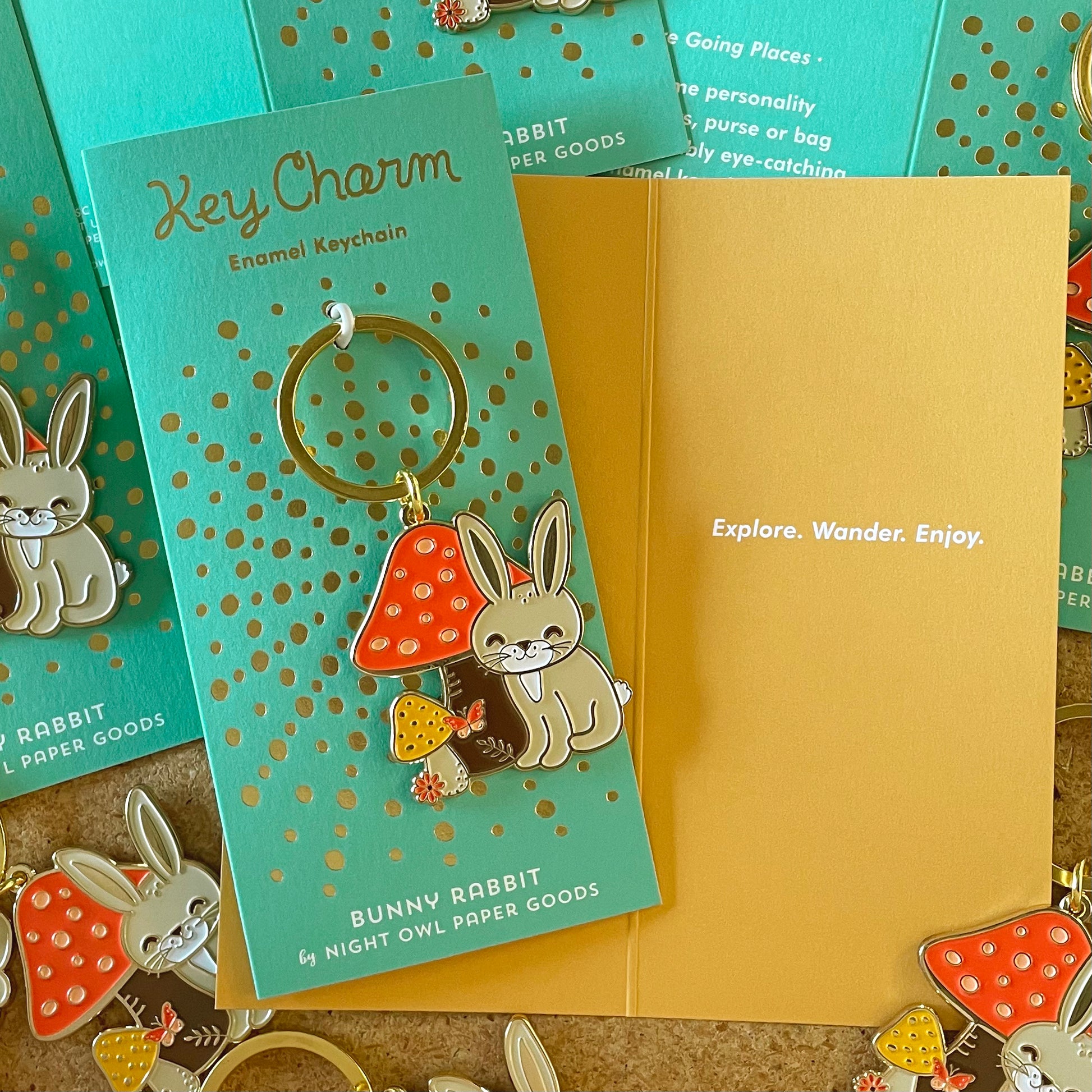 Rabbit with mushroom keychain on gold foil-stamped backer cards with inside text that reads Explore. Wander. Enjoy.