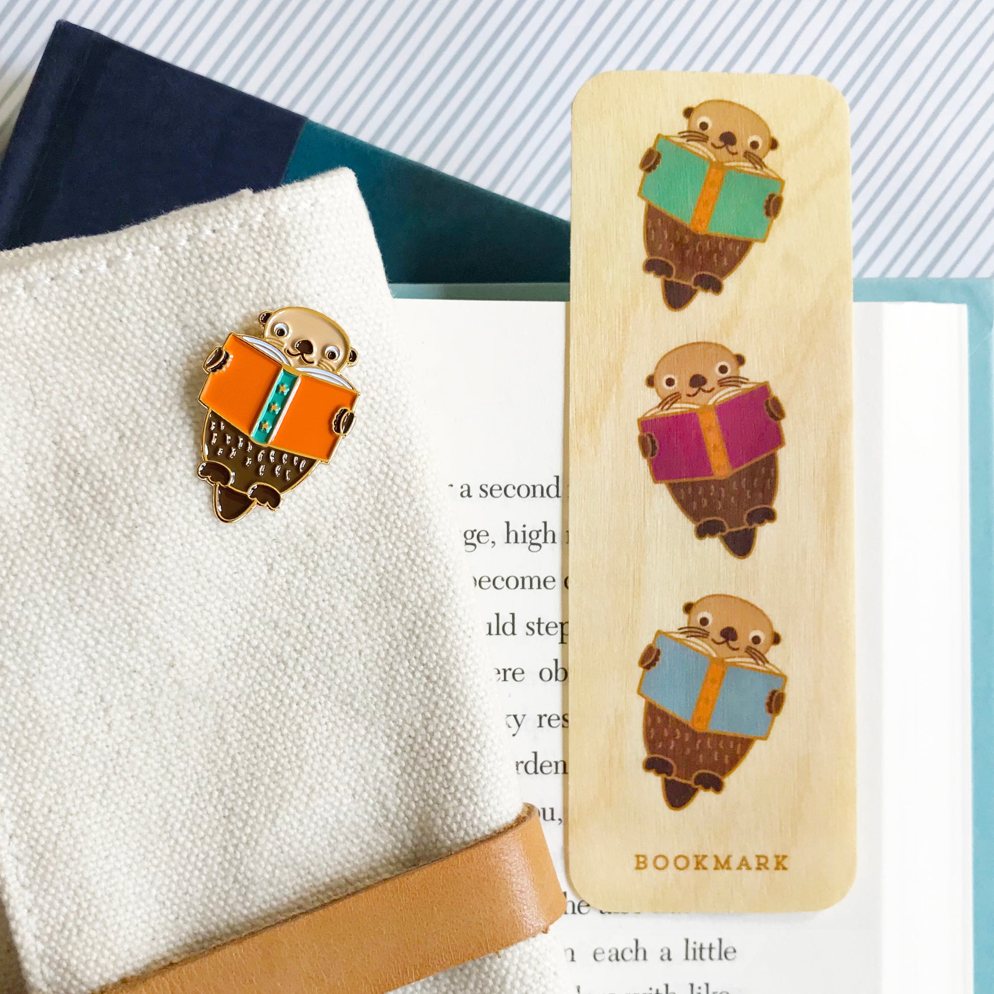 Enamel pin of an otter reading a book and wooden bookmark with three otters reading books.