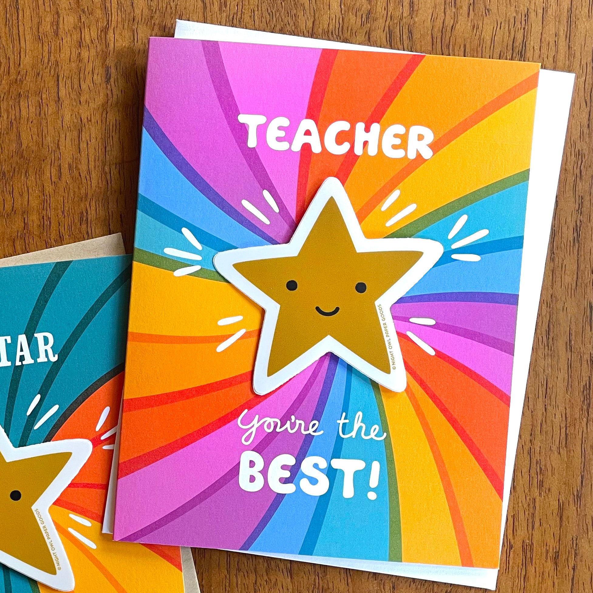 Colorful rainbow card with a removable gold star vinyl sticker and 'Teacher You're the Best!' text displayed on a wooden surface
