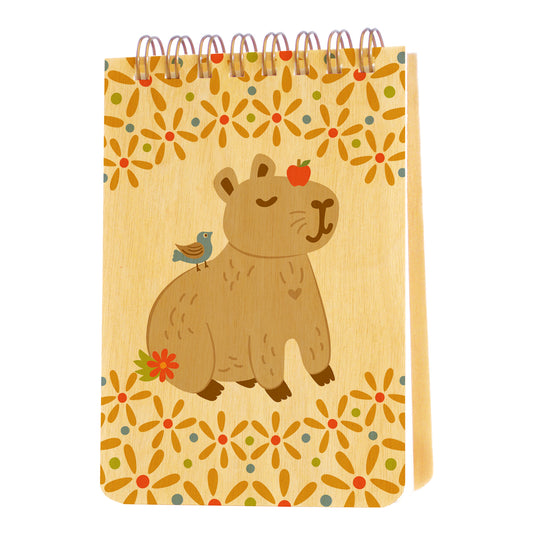 Mini notepad with birch wood covers, spiral binding at top and a content capybara with an apple on its head and a bird on its back, surrounded by floral designs