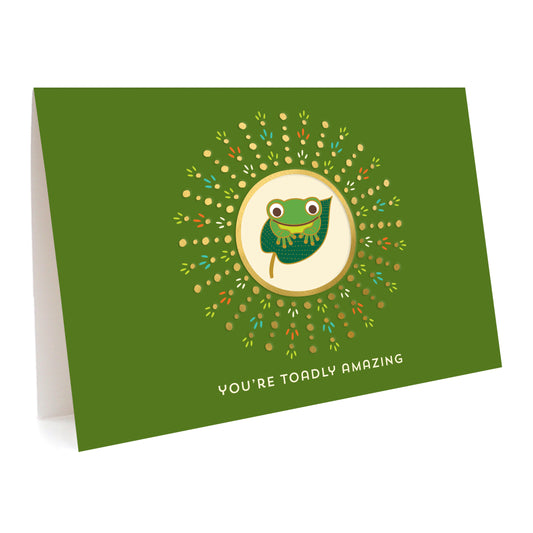 Green greeting card with a happy frog illustration and gold foil accents. Text reads 'You're Toadly Amazing.'