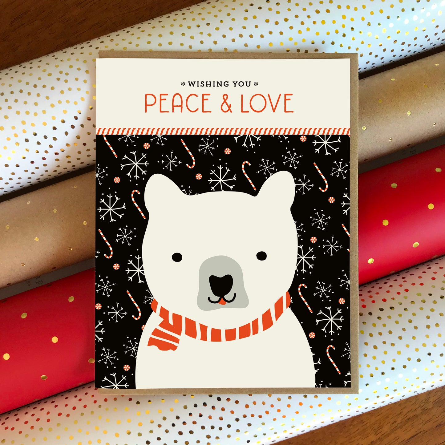Holiday card with a polar bear wearing a red and white scarf on  black background with white snowflakes and candy canes. Sentiment reads 'Wishing you peace & love'.