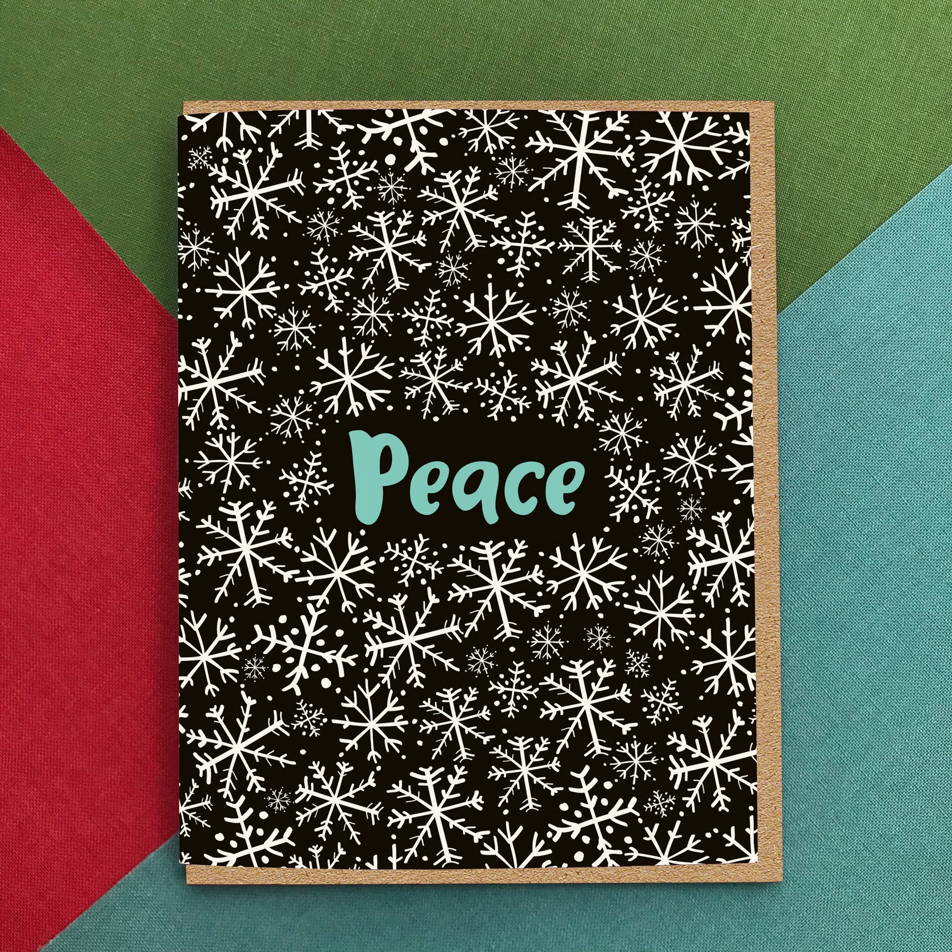 Black holiday greeting card with a playfully illustrated snowflake pattern and 'Peace' text. Background of photo is colorful.