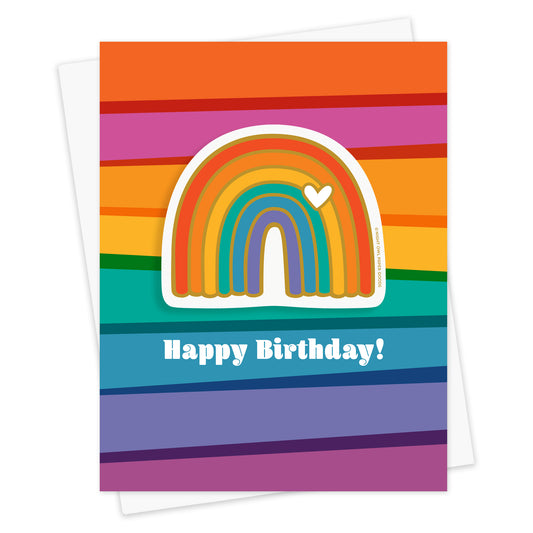 Front of birthday greeting card with a removable rainbow vinyl sticker and "Happy Birthday!" text surrounded by colorful rainbow, star, and heart designs on a bold rainbow striped background. Shown with a white envelope.