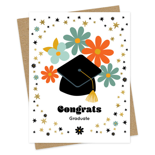 Graduation card with a mortarboard cap and "Congrats Graduate" surrounded by gold foil stars and pastel flowers on a white background. Shown with a kraft envelope.