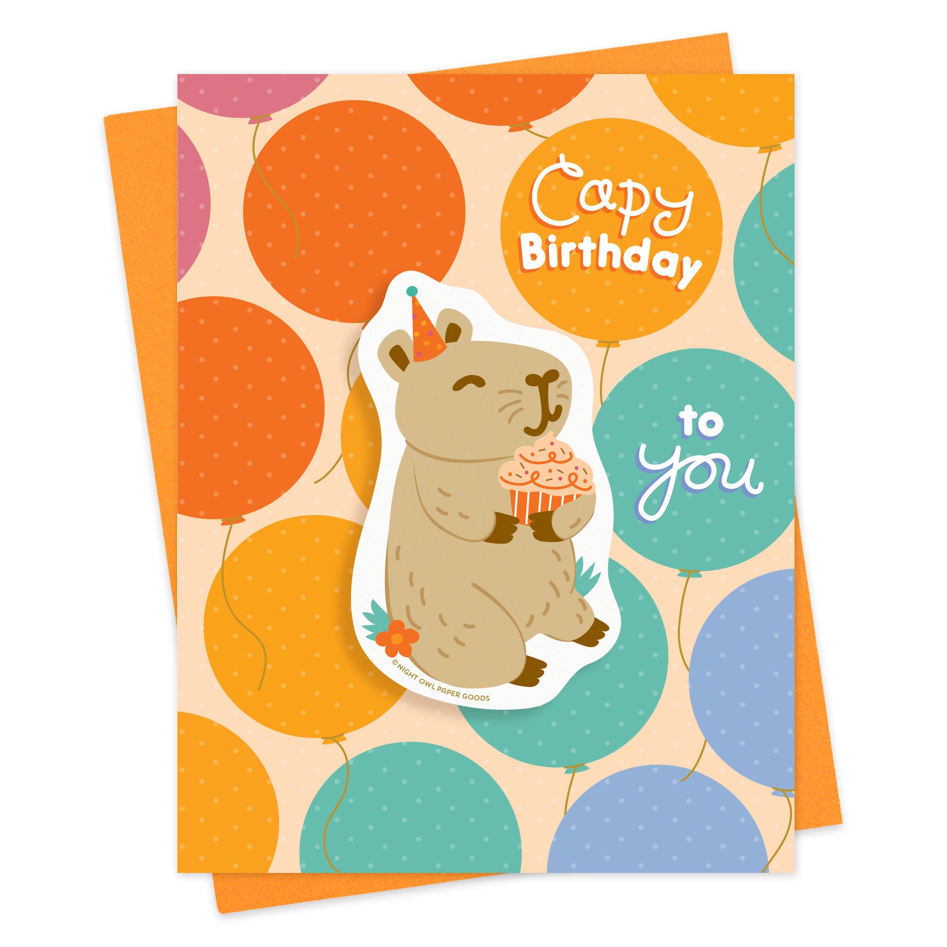 Birthday card with colorful balloons and “Capy Birthday to You” greeting featuring a removable vinyl sticker of a capybara wearing a party hat and holding a cupcake. Pictured with an orange envelope.