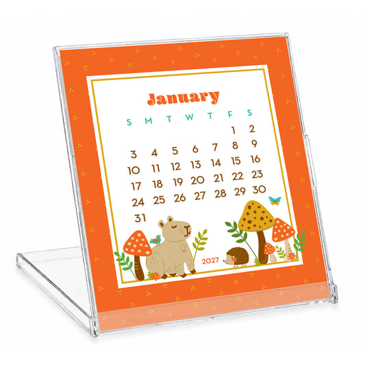 2027 Forest Friends Woodland Animals & Gnomes Desk Calendar with clear stand. January is shown, featuring a capybara and hedgehog sitting in a mushroom forest. The rest of the calendar features colorful woodland animals, cheerful gnomes, mushrooms, flowers and plants in a whimsical illustrated style. The compact calendar is displayed in a reusable clear jewel case that doubles as a stand.
