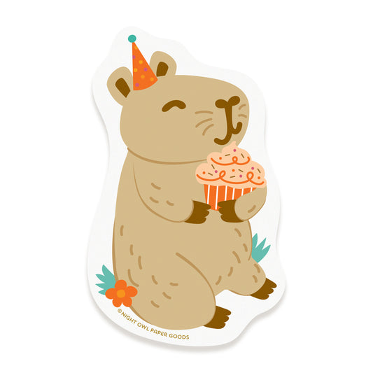 Cute capybara vinyl sticker wearing a colorful party hat and holding a frosted cupcake.