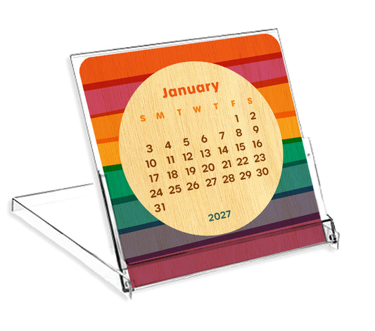 Birch wood mini desk calendar with bold horizontal rainbow stripes displayed in a clear reusable jewel case stand, showing the January 2027 calendar page.