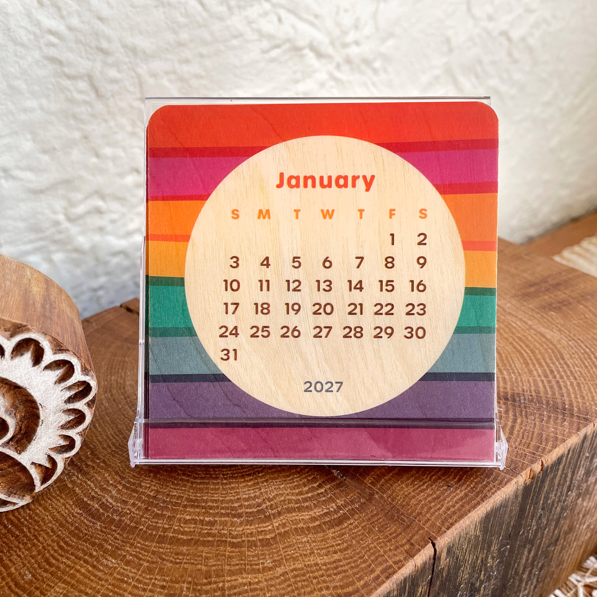 Real wood mini desk calendar with vibrant stripes in a rainbow of colors. Calendar sits in the clear display case that it comes with.