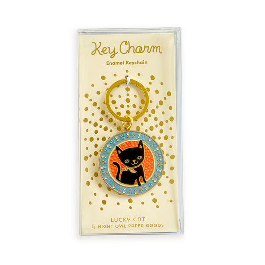 Black cat enamel keychain on gold foil stamped backer card packaged in a clear gift box. Pale yellow backer card reads "Key Charm Enamel Keychain" at top and "Lucky Cat by Night Owl Paper Goods" at bottom.