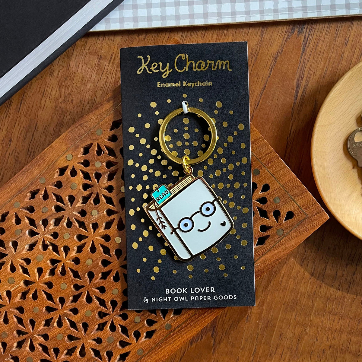 Book Lover enamel keychain on gold foil stamped backer card. Black backer card reads "Key Charm Enamel Keychain" at top and "Book Lover by Night Owl Paper Goods" at bottom.