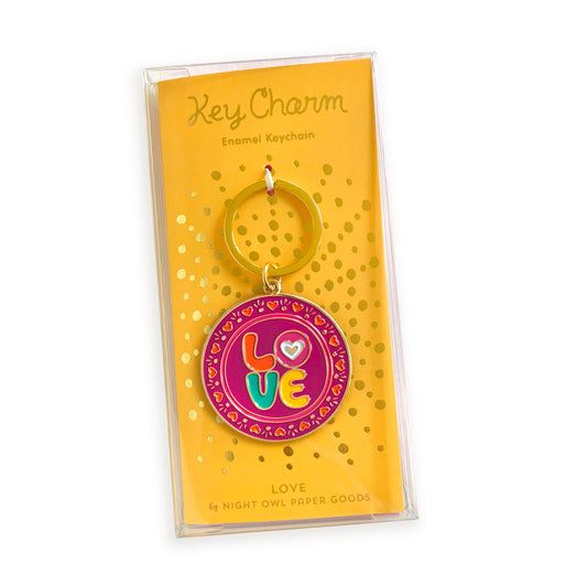 Love enamel keychain on gold foil stamped yellow backer card packaged in a clear gift box. Backer card reads "Key Charm Enamel Keychain" at top and "Love by Night Owl Paper Goods" at bottom.