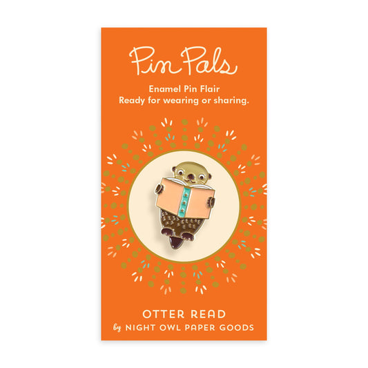 Enamel pin of an otter reading a book mounted on an orange backer card