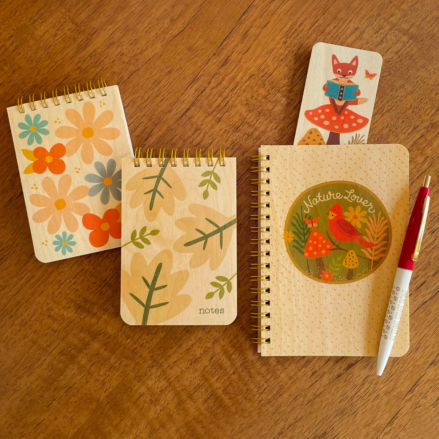 Nature Lover notebook featuring a red bird and forest scene, two mini notepads with wood covers featuring colorful flowers and leaves, a Reading Fox bookmark and a ballpoint pen.
