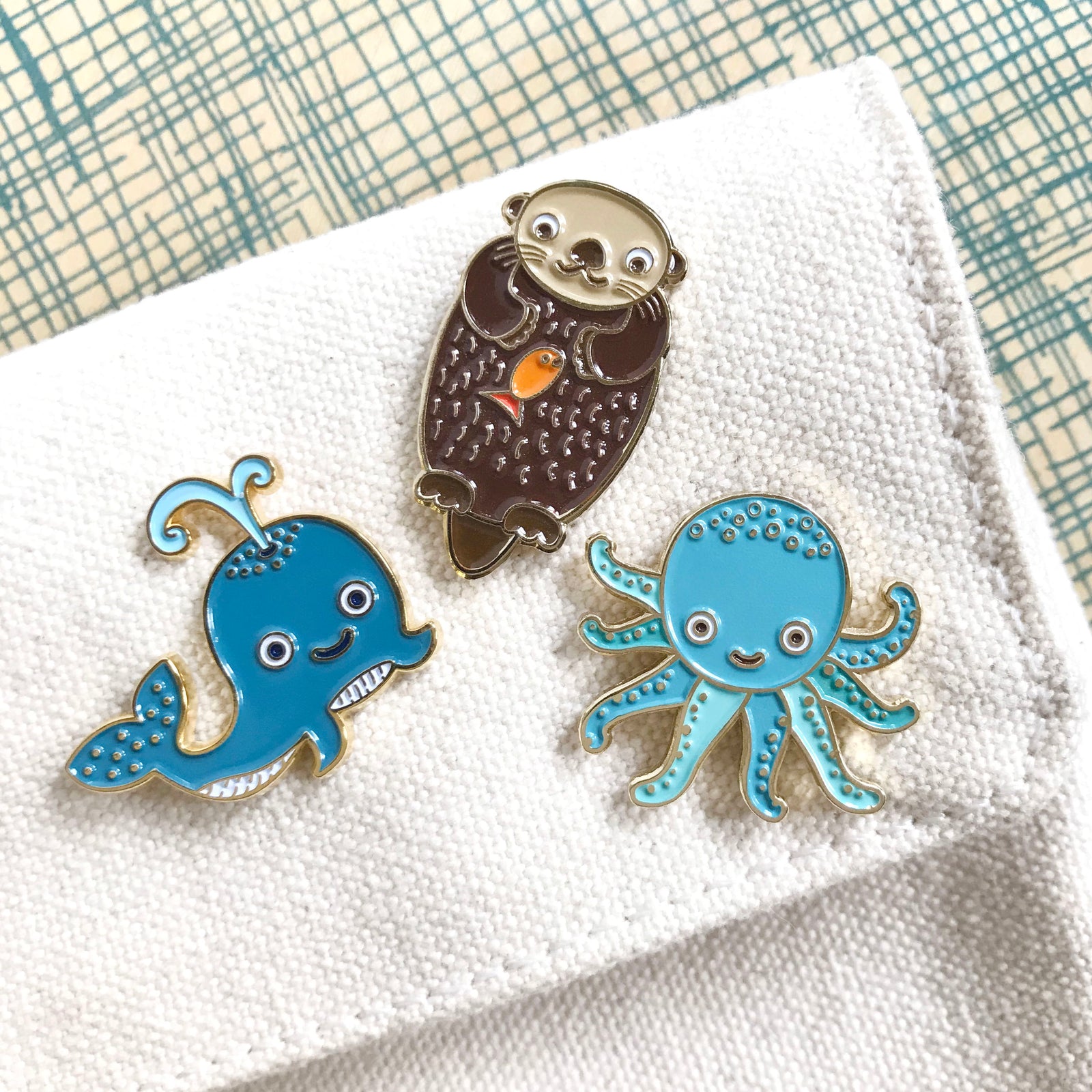 Sea Critter Flair Pin Pals Gift Set pins - Three enamel pins of an otter, a whale, and an octopus on canvas with a checkered background.