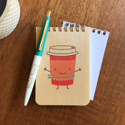 Fun mini wood notepad with cute illustration of a to-go cup of coffee with smile and cute belt. Click pen is teal with gold accents and reads ' Magic Wand'.