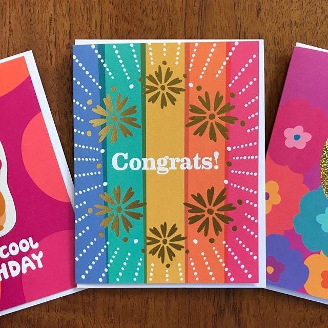 Colorful pastel striped greeting card with gold foil floral designs and 'Congrats!' text.