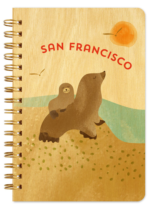 Spiral-bound wood notebook with birch wood covers featuring two sea lions on a sunny beach with ocean waves and "San Francisco" text.