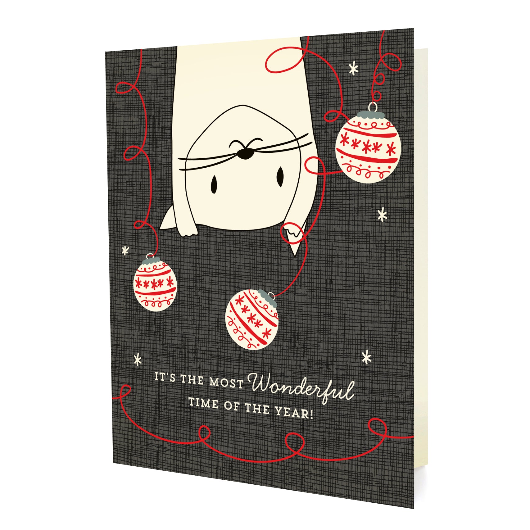 Front of folded holiday card featuring a playful cat swinging from the top among Christmas ornaments with “It’s the most wonderful time of the year!” text on a textured background.