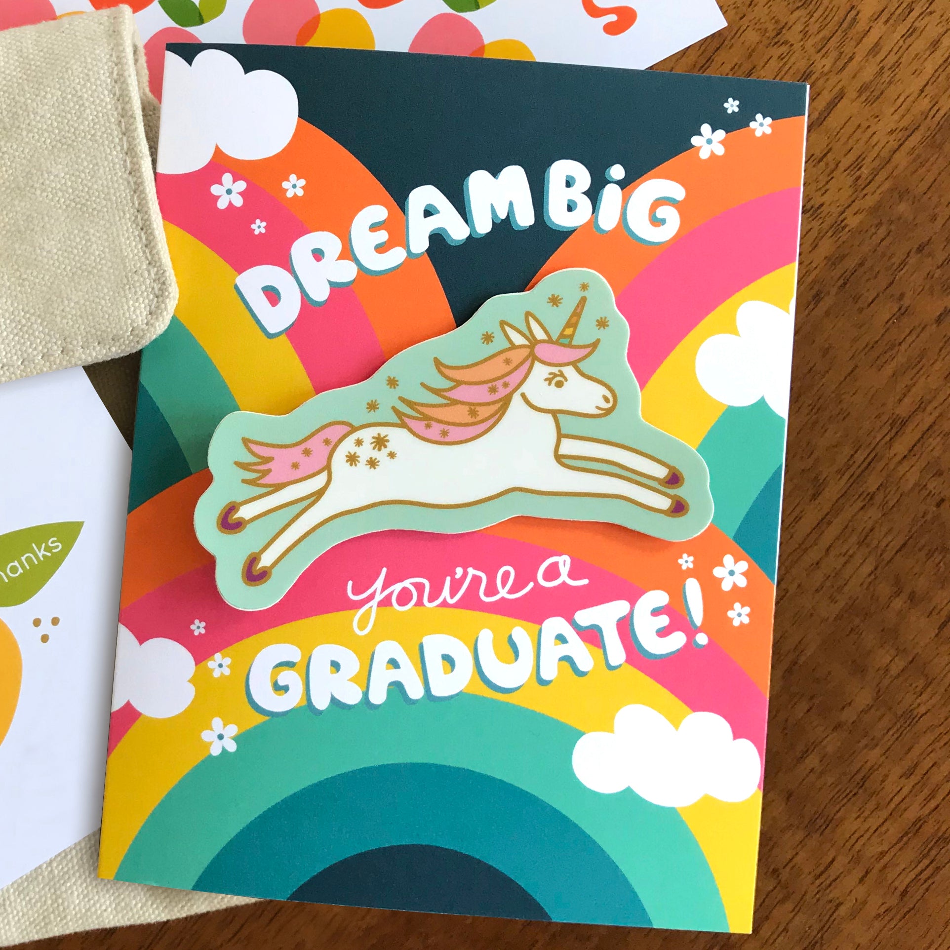 Colorful graduation card with a unicorn and rainbow design. Unicorn has pastel rainbow horn and is a removable vinyl sticker.